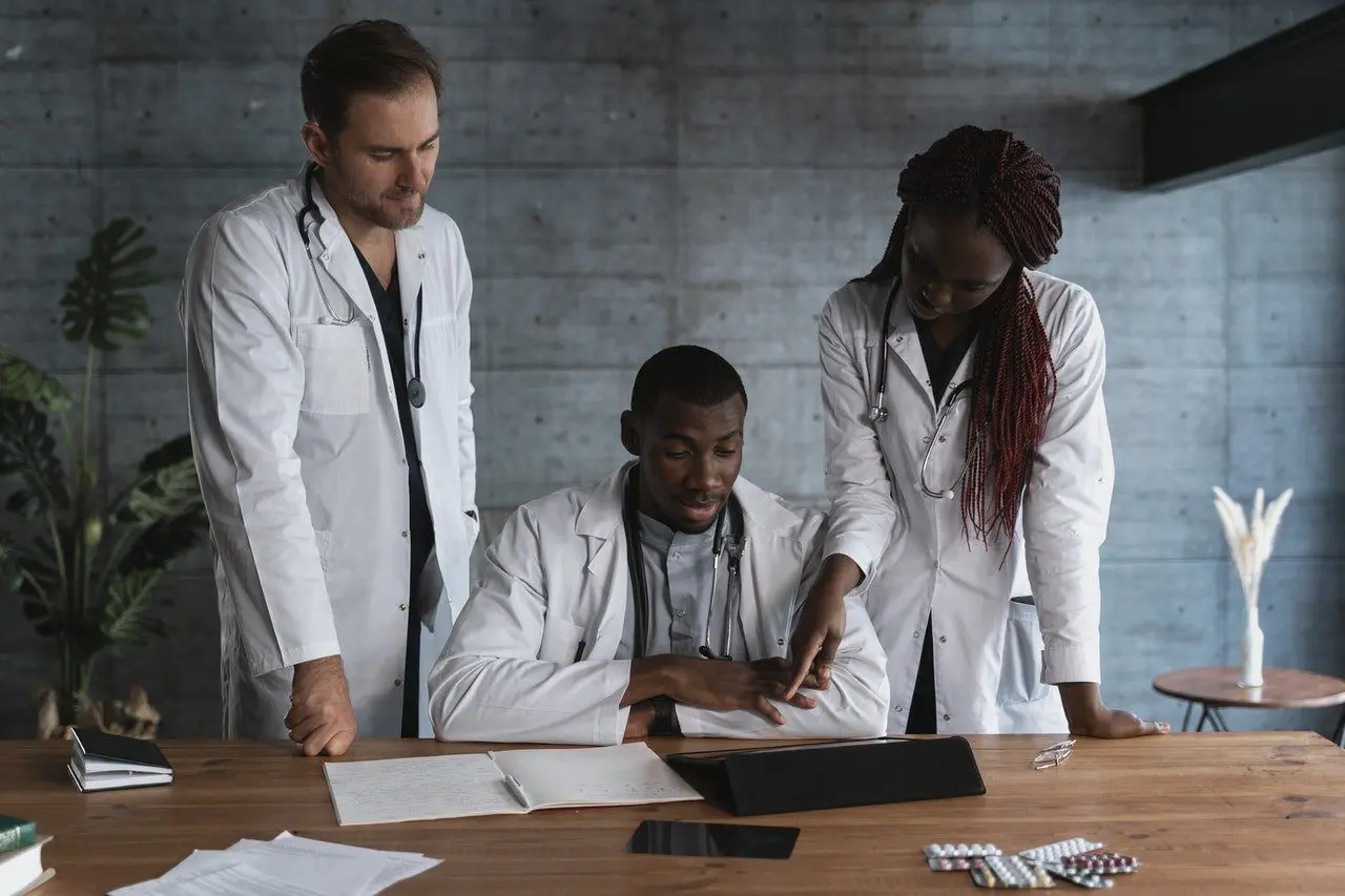 Three doctors are gathered around a table looking at something.