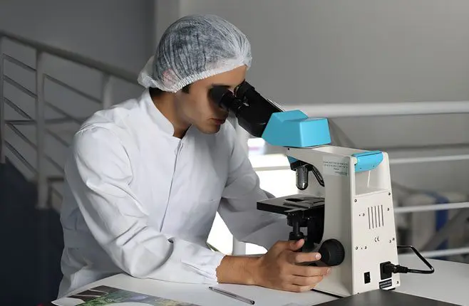 A man in white lab coat looking through microscope.