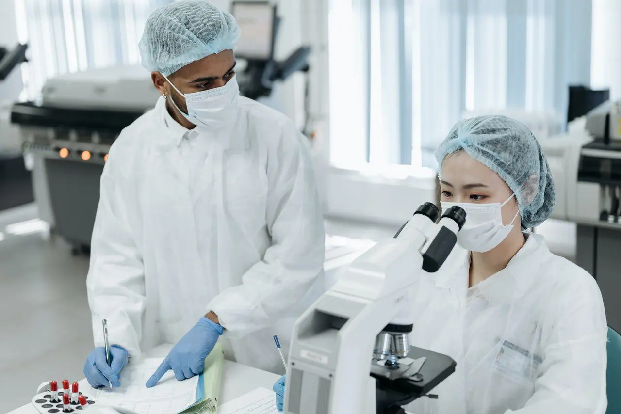 Two doctors in white lab coats and masks working with a microscope.