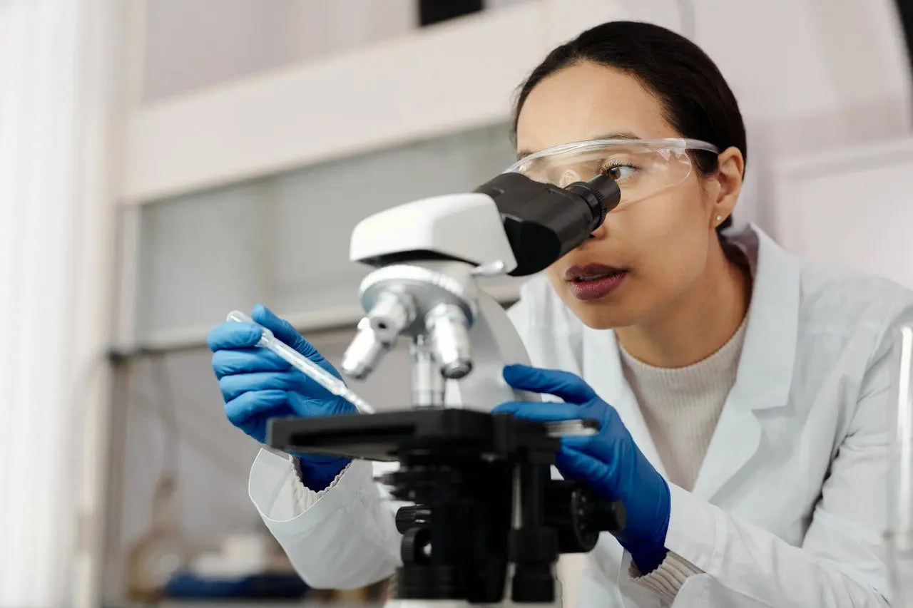 A woman in lab coat looking through microscope.
