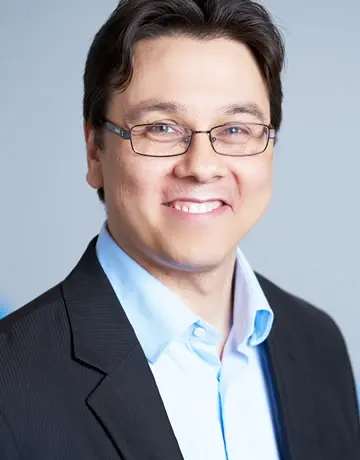 A man in glasses and a suit smiling for the camera.
